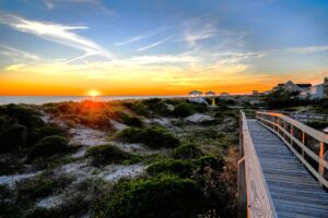 A walkway along the sand dunes with the sun setting over the ocean.